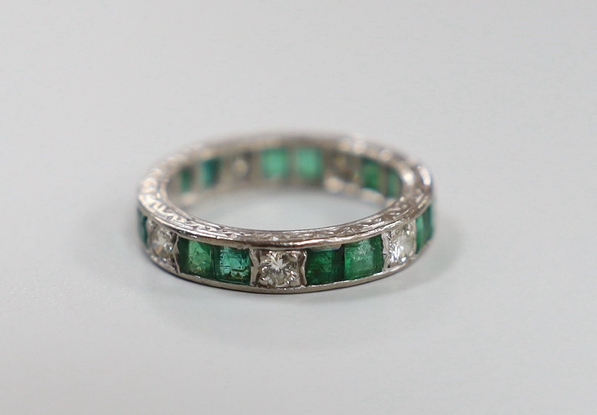 A mid 20th century 18ct white metal, emerald and diamond set full eternity ring (a.f.), size M/N, gross weight4.9 grams.